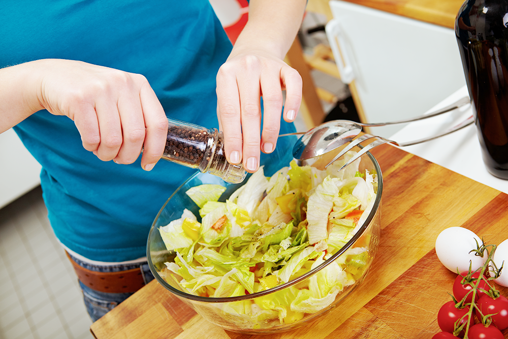 Ein Mann würzt einen Salat mit Pfeffer