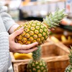 Eine Frau sucht sich im Supermarkt eine Ananas aus.