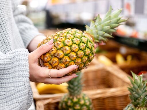 Eine Frau sucht sich im Supermarkt eine Ananas aus.