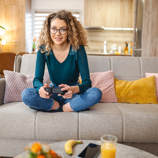 Female gamer sitting on sofa. Banana and orange Juice in front of her on the couch table.